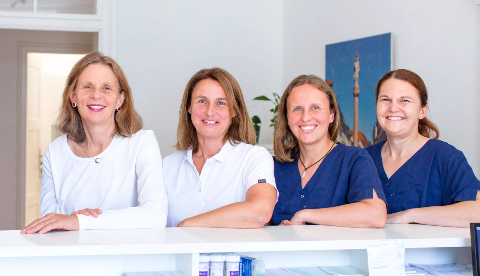Die zwei Frauenärztinnen und zwei MFAs stehen am Empfangstresen in der Praxis